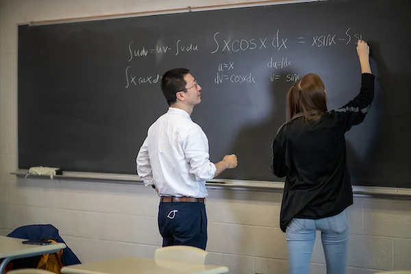 Students working out formula on chalkboard with professor
