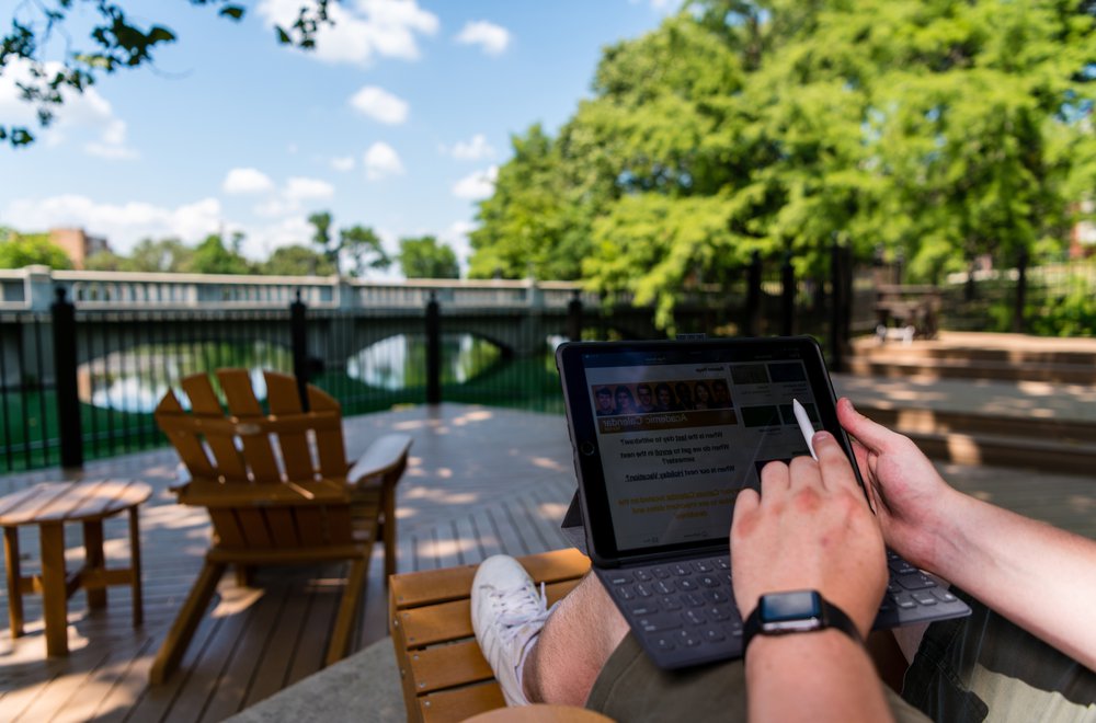Student working on laptop in front of Emporia State's Wooster Lake