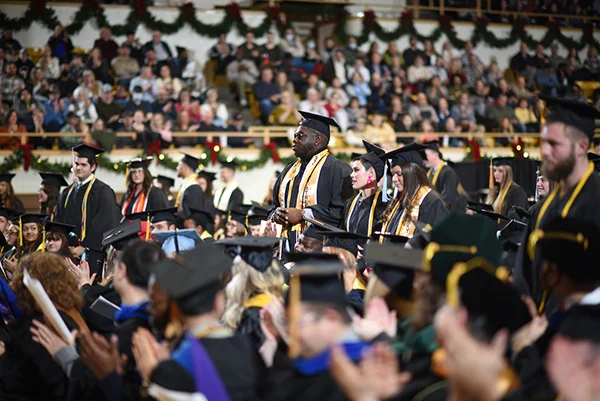 Students both standing and seated in caps and gowns for graduation.