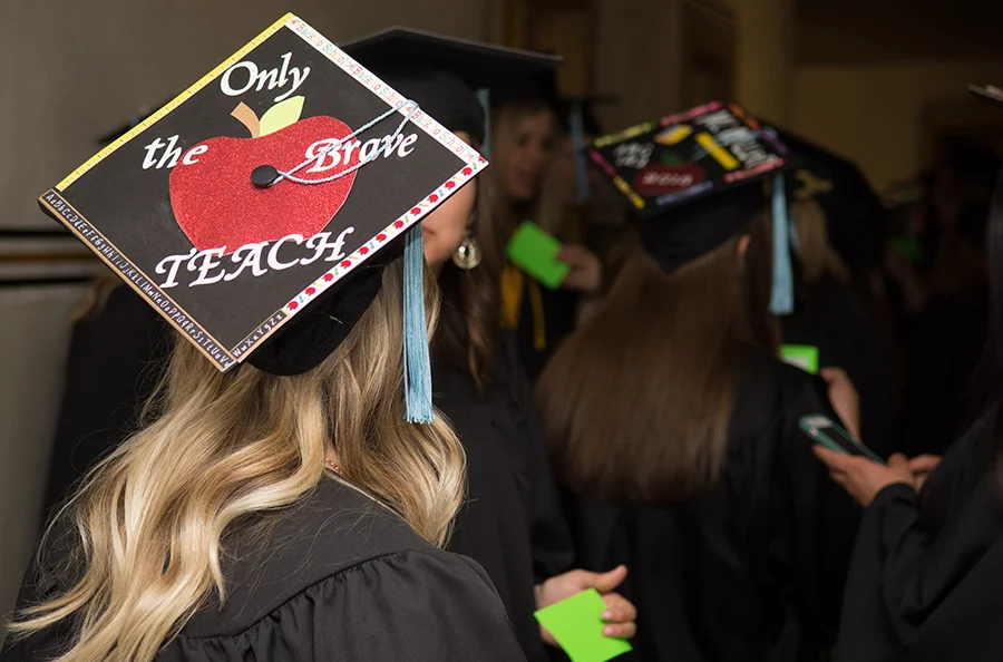 Student wearing graduation hat that reads "Only the brave teach"