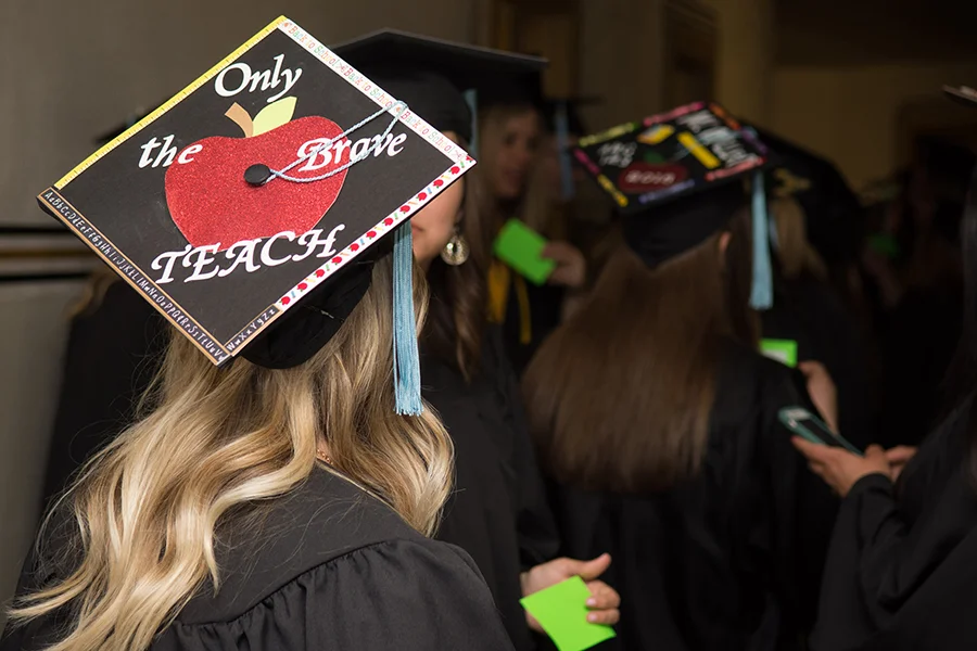 Student wearing graduation hat that reads "Only the brave teach"
