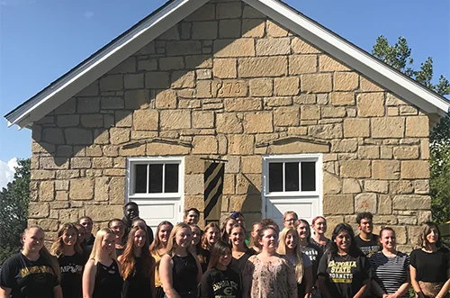 Students posing for photo in front of one-room schoolhouse at Emporia State