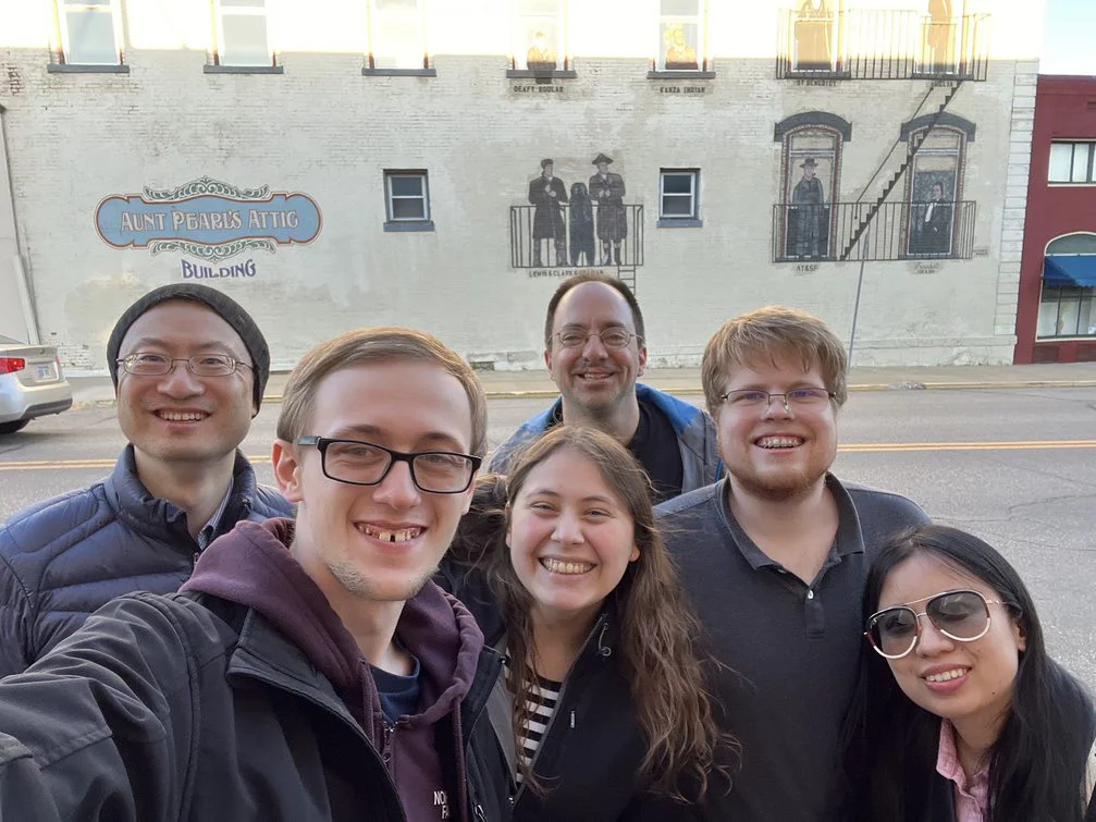 Four students and two professors are standing in front of a building that says "aunt pearl's attic.