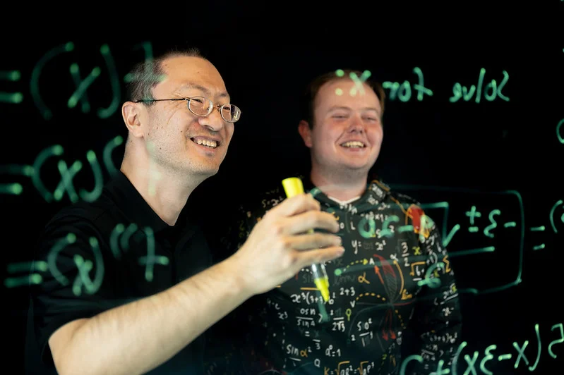 Professor and Mathematics student solving equation on light board