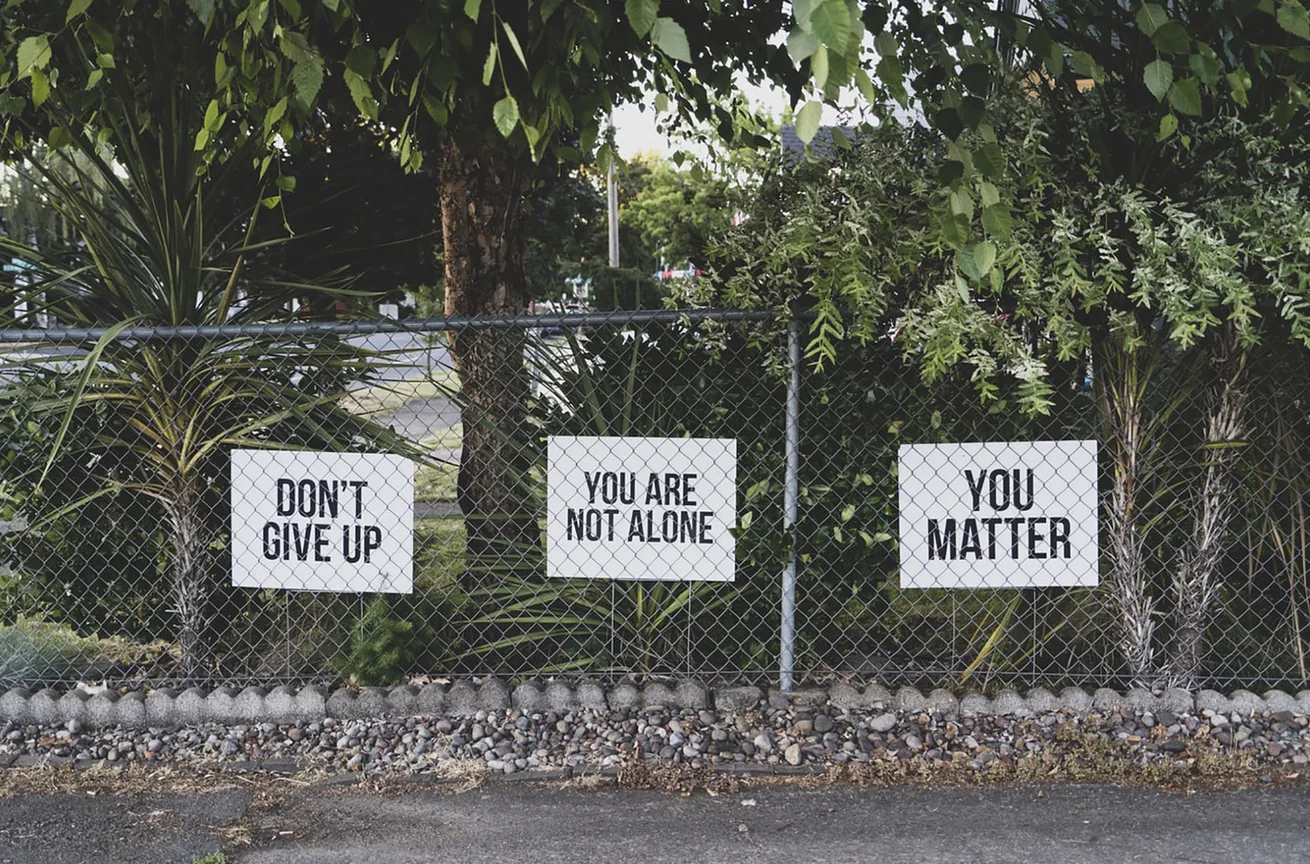 Signs on fence reading "don't give up," "you are not alone," "you matter"