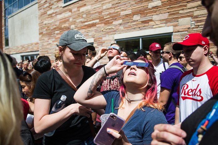 Woman wears solar eclipse glasses and looks up at the sky.