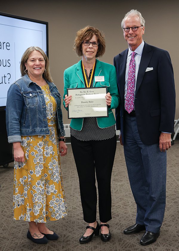 3 people standing together. Middle person, a woman, hold a framed certificate.