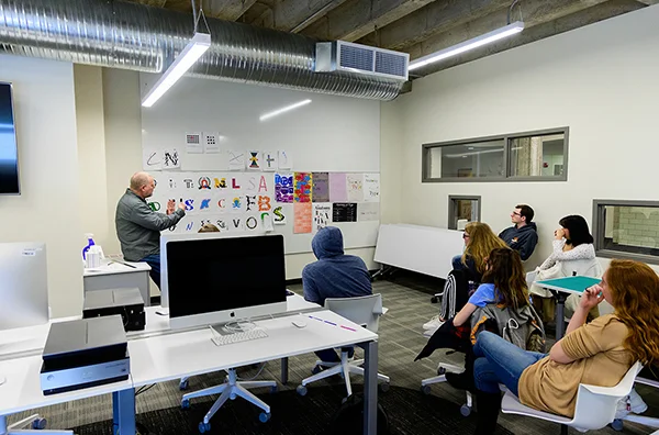 Students seated watching professor at white board demonstrating graphic design