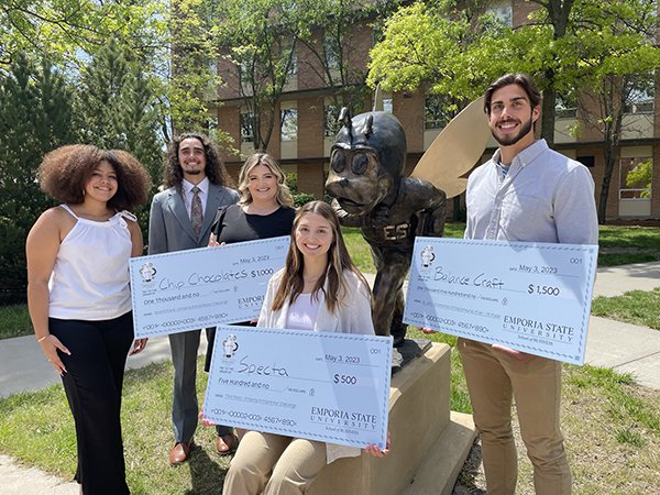 Five students hold large presentation checks