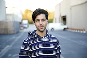 Man with dark hair wearing striped shirt poses for photo