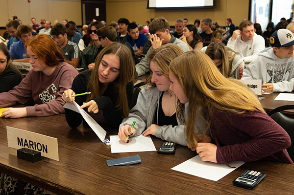 Three high school girls sit at a table and look over an answer on a math worksheet.