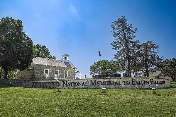 Landscape photo with limestone wall in foreground and schoolhouse in background.